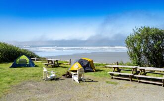 Two tents and picnic tables on grassy area overlooking Kalaloch Beach and ocean under a clear blue sky.