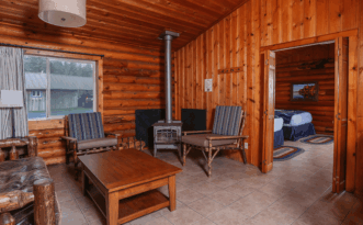 Kalaloch Cabin living room with wood stove, rustic chairs, coffee table, and view into bedroom.