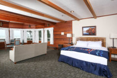Kalaloch Suite room with a large bed, couch, chairs, wood-paneled walls, and windows overlooking the ocean.