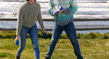Two people playing bean bag toss on grass at Olympic Peninsula, smiling and enjoying a sunny day.