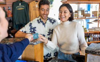 Smiling woman hands a card to a cashier, with a man standing beside her at a counter.