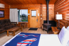 Kalaloch Cabin room with wood stove, rustic furniture, and a bed with a colorful fish blanket.