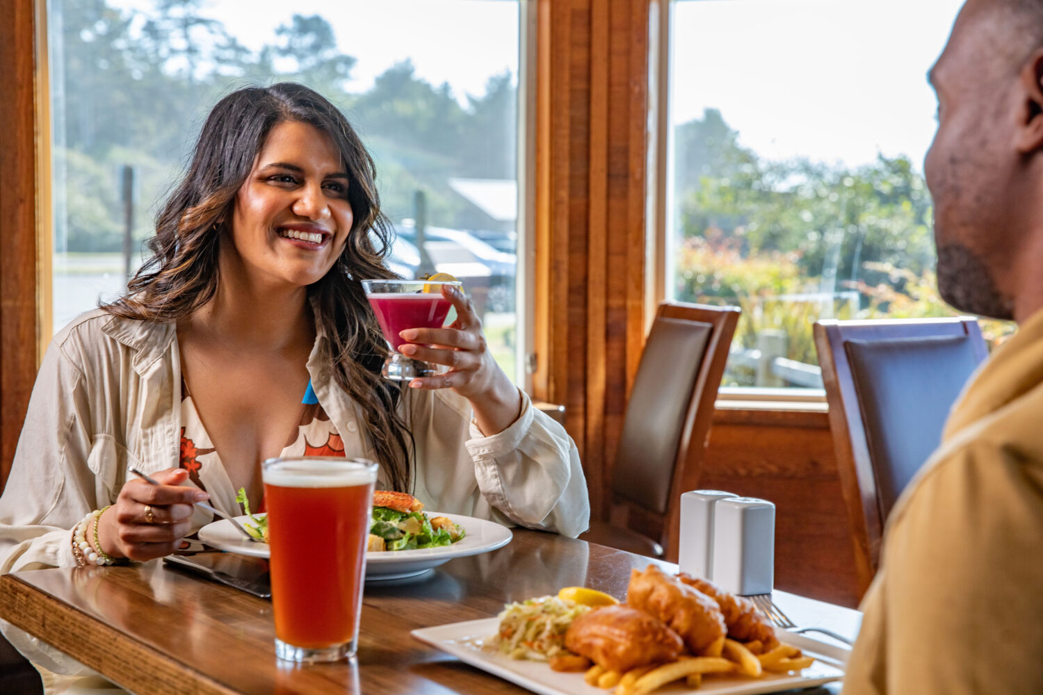 A woman smiles, holding a cocktail, while dining with a man at Creekside Restaurant.
