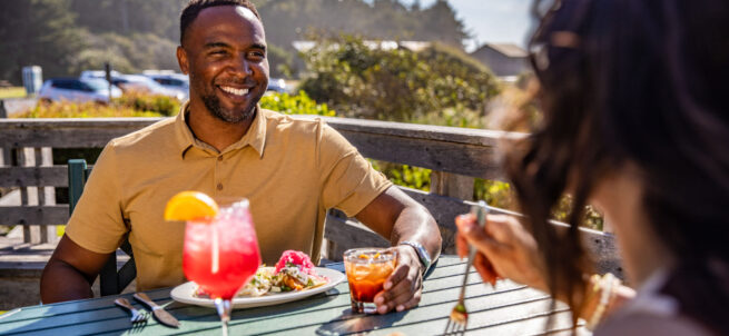 A man smiles at a woman while they dine outdoors at Creekside Restaurant on a sunny day.