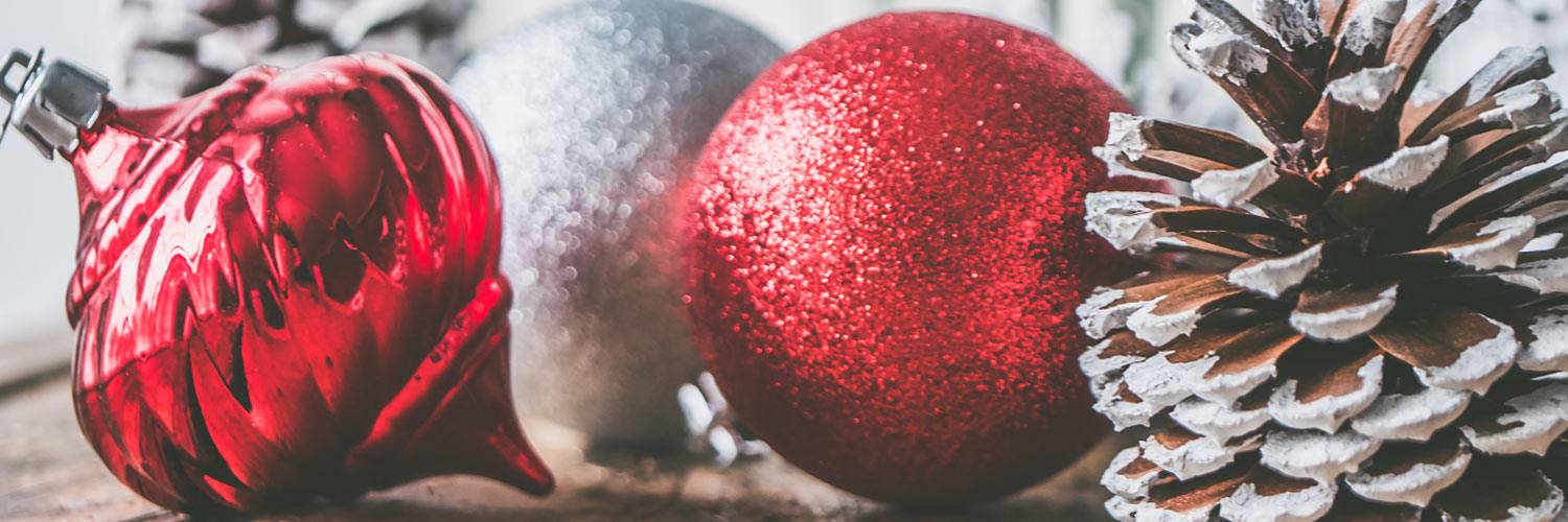 Red and silver Christmas ornaments sit on a wood surface with pine cones
