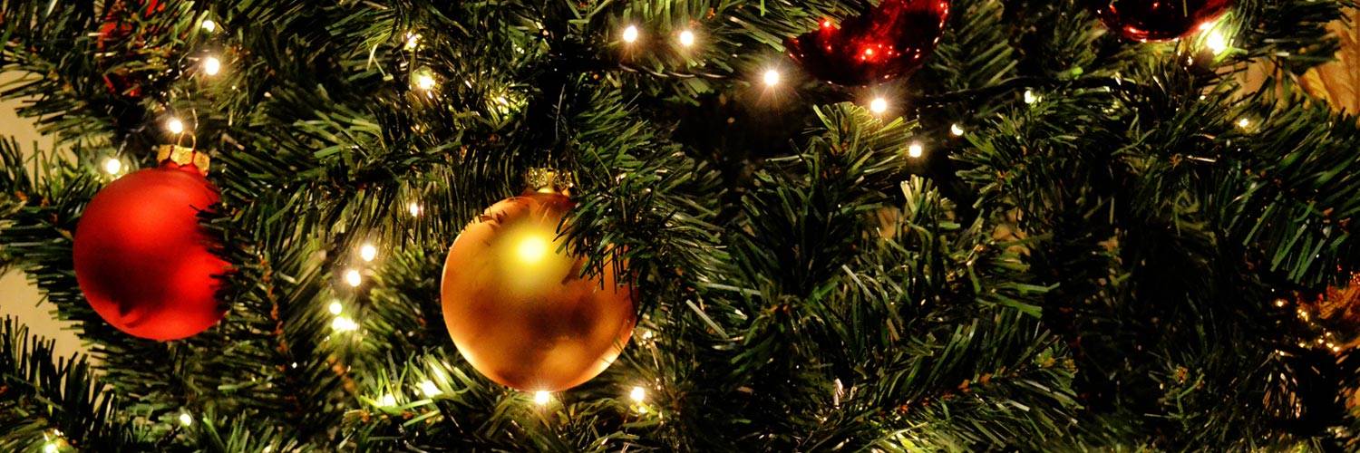 Red and gold ball ornaments hang on a Christmas tree with lights