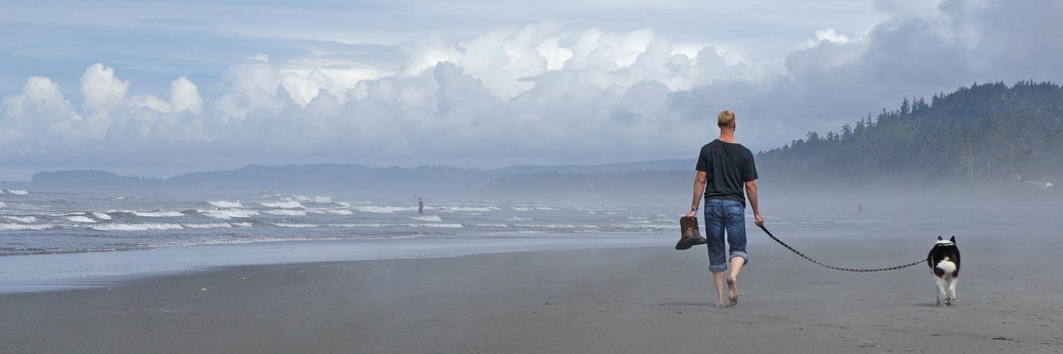 A man walks his dog on a beach near Kalaloch Lodge
